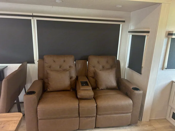 Comfortable RV rental interior featuring a brown recliner sofa with cup holders & windows with black blinds, ideal for relaxing.. Forest River Grand Surveyor 2025
