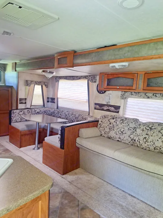Inside an rv rental: Cozy living area with a U-shaped dinette, sofa, overhead cabinets, and a kitchen counter.. Keystone RV Passport Ultra Lite 2012