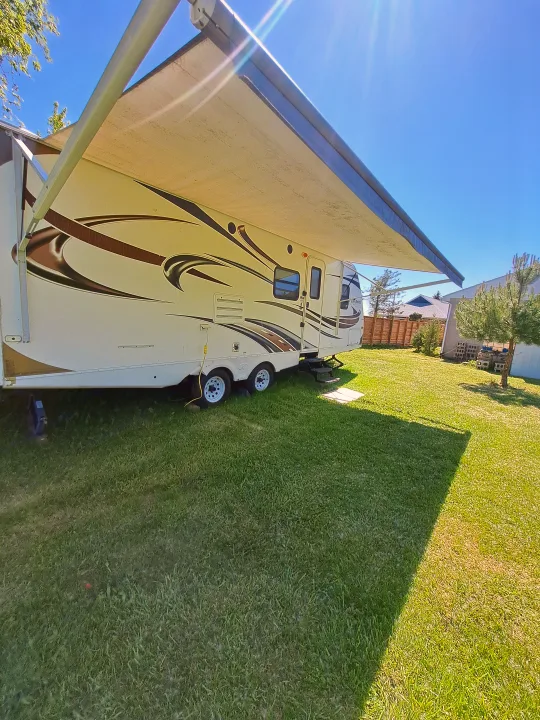 White RV rental with brown and black swirl graphics, awning extended, parked on a sunny green lawn, ready for outdoor adventure.. Keystone RV Passport Ultra Lite 2012