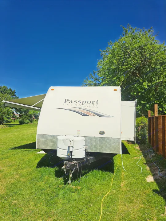 A white Passport Ultra Lite travel trailer rv rental parked on green grass under a clear blue sky, ready for adventure.. Keystone RV Passport Ultra Lite 2012