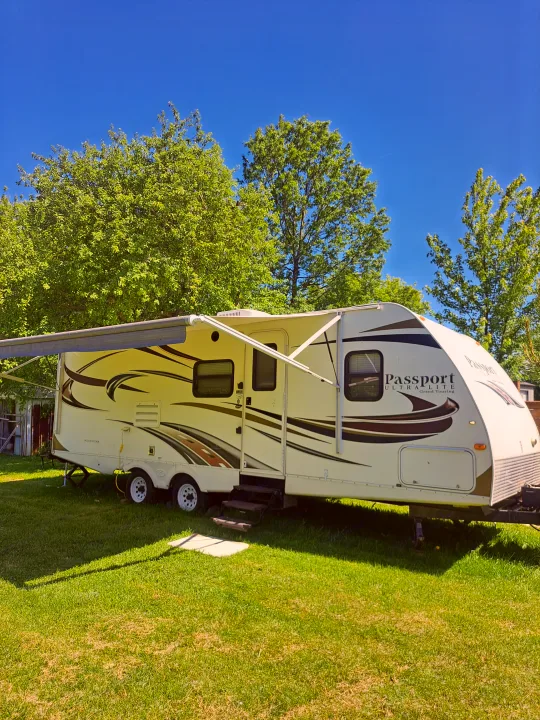 Spacious Passport travel trailer, an excellent RV rental choice. Parked on green grass with extended awning, under a clear blue sky.. Keystone RV Passport Ultra Lite 2012