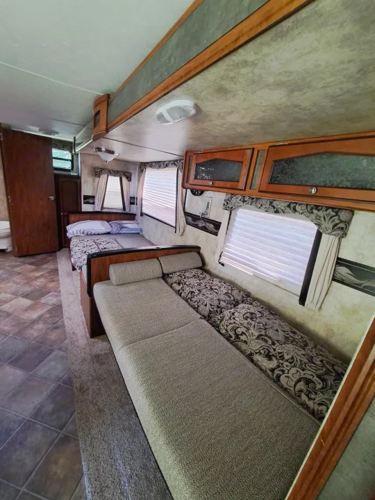 This RV rental interior shows a cozy living/sleeping area with multiple beds, overhead cabinets, and windows with blinds.. Keystone RV Passport Ultra Lite 2012