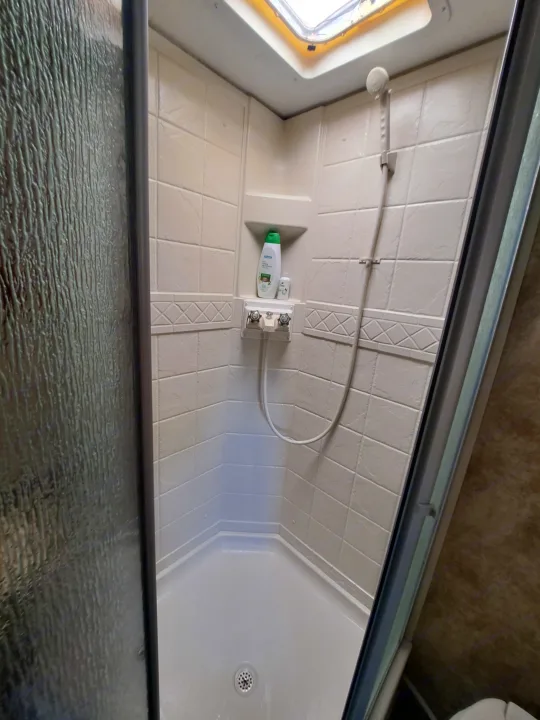 Compact RV rental shower with textured glass door, handheld shower, and toiletries shelf. Clean and ready for your adventure.. Keystone RV Passport Ultra Lite 2012