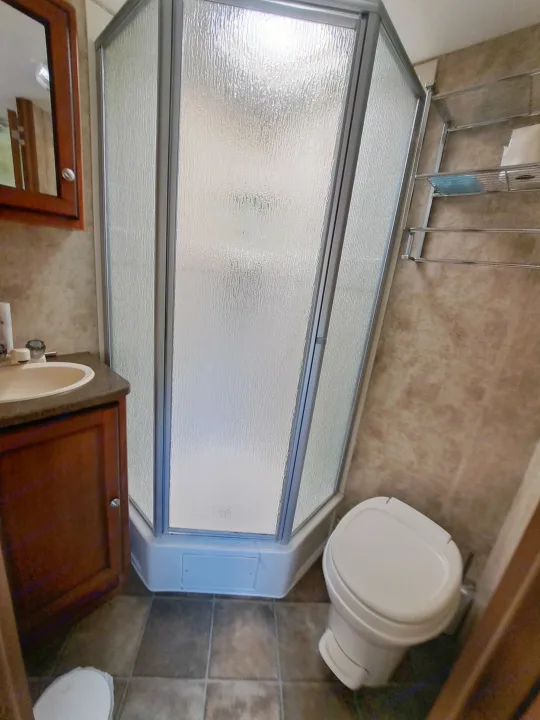 RV rental's compact bathroom features a corner shower (frosted glass), toilet, and sink vanity.. Keystone RV Passport Ultra Lite 2012