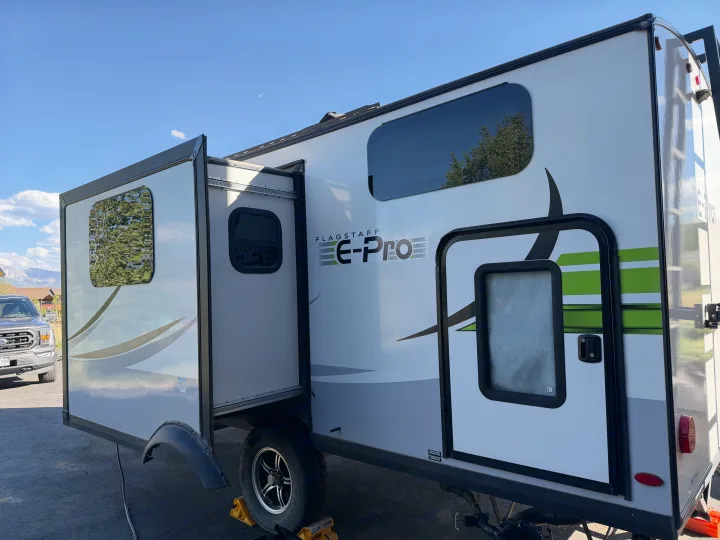 This Flagstaff E-Pro rv rental, a white and gray travel trailer with an extended slide-out, is parked on a sunny day.. Forest River Flagstaff E-Pro 2022