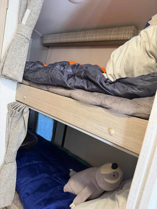 Inside an RV rental: cozy bunk beds with sleeping bags, blankets, and a plush sloth on the lower bunk.. Forest River Flagstaff E-Pro 2022