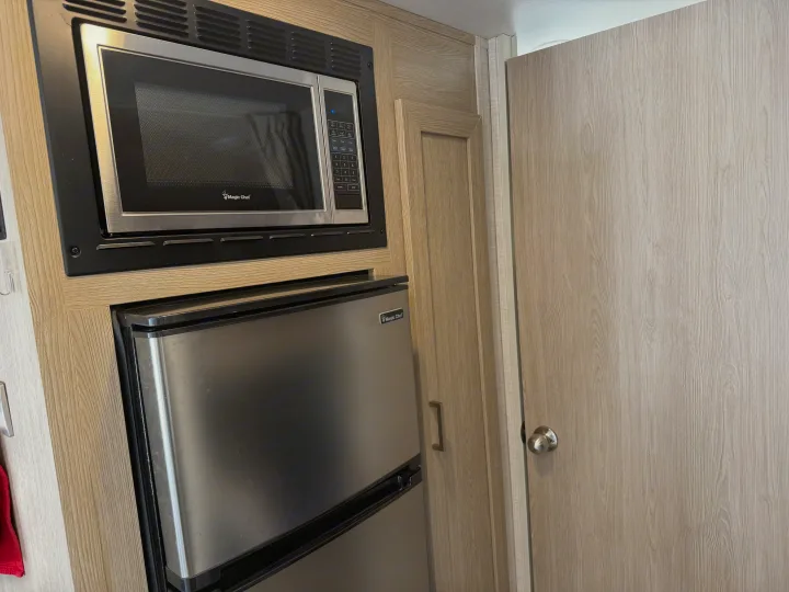 RV rental kitchen features Magic Chef stainless steel microwave and fridge, built into light wood cabinets next to a door.. Forest River Flagstaff E-Pro 2022
