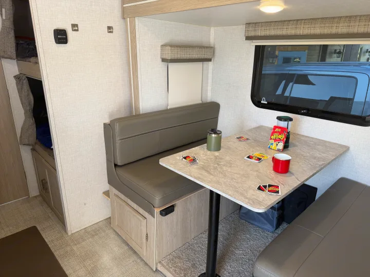 Cozy dinette in an RV rental, set for a game of UNO. Features bunk beds, a thermostat, and a window view for travel comfort.. Forest River Flagstaff E-Pro 2022