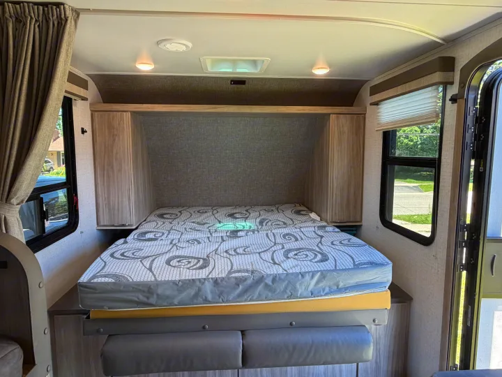 Cozy RV rental bedroom features a convertible bed, overhead cabinets, windows with blinds, and ceiling lighting.. Minnie Micro Minnie 2021