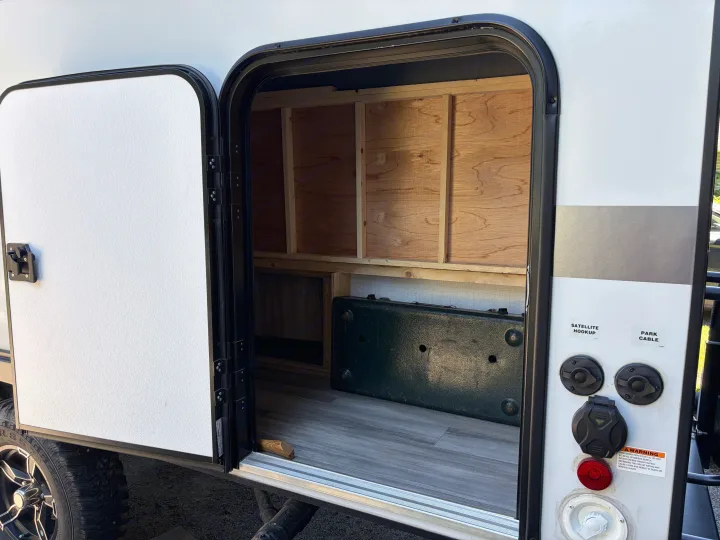 RV rental pass-through storage bay, detailed with wood shelving and external electrical, satellite, and cable hookups.. Minnie Micro Minnie 2021
