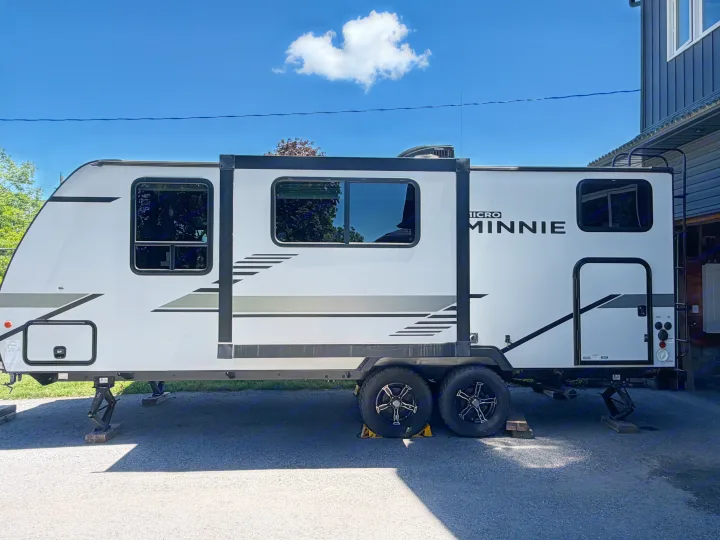 Side view of a white Micro Minnie RV rental travel trailer parked with leveling jacks on a sunny day.. Minnie Micro Minnie 2021