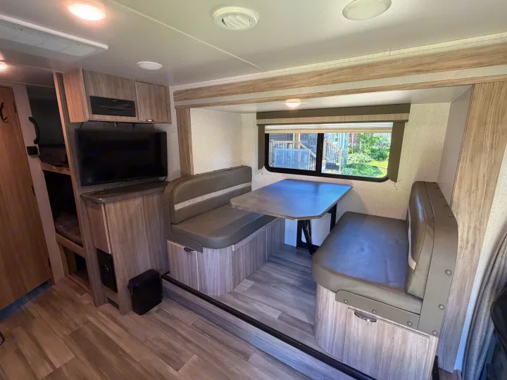 RV rental interior featuring a cozy dinette with a table and booth seating, a TV, and visible bunk beds on the left.. Minnie Micro Minnie 2021