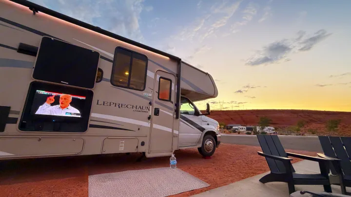 RV rental: Relaxing outdoors with an RV featuring an exterior TV, chairs, and scenic sunset views in an arid park.. Coachmen Leprechaun 2021