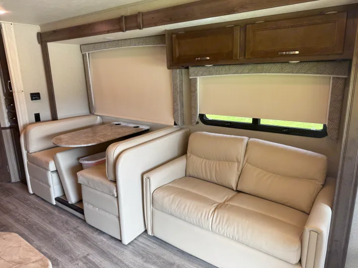 Comfortable RV rental interior: cream dinette, matching sofa, wood cabinets, and large windows with blinds for privacy.. Entegra Coach Vision 2020