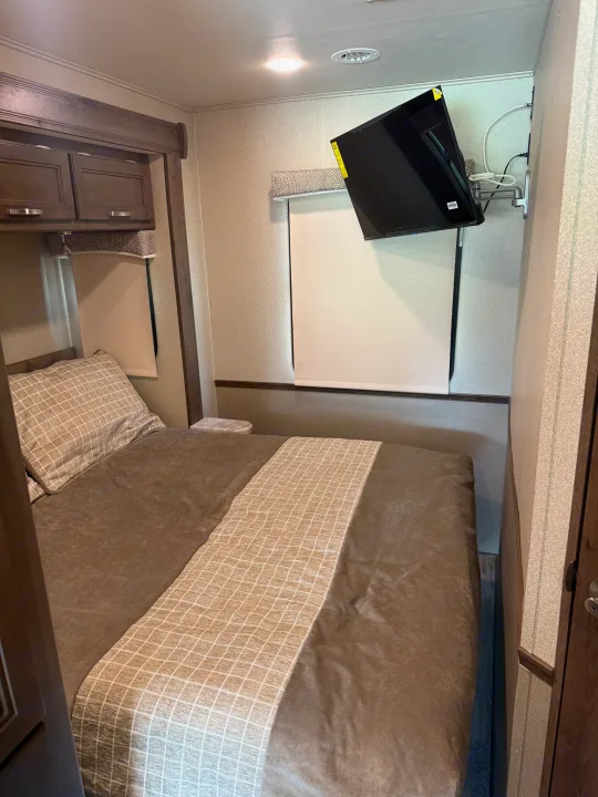 Cozy rv rental bedroom with a bed, overhead cabinets, window, and wall-mounted TV. Perfect for your next adventure.. Entegra Coach Vision 2020