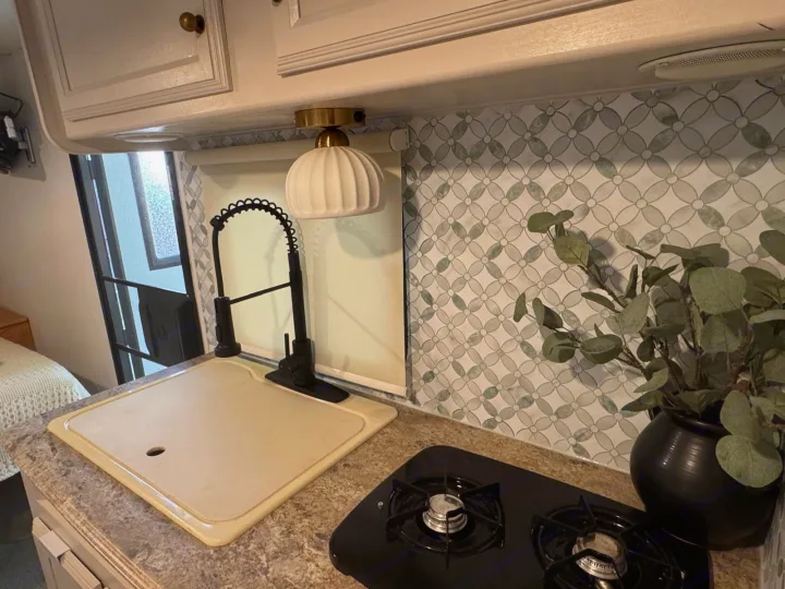 Modern rv rental kitchen with green geometric backsplash, black faucet, stove, and light fixture.. Coachmen Apex 2017