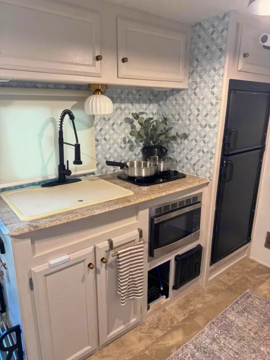 This compact rv rental kitchen features a black gooseneck faucet, light gray cabinets, patterned backsplash, microwave, fridge, and induction cooktop.. Coachmen Apex 2017