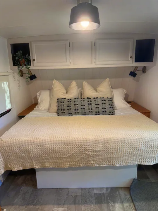 Cozy RV rental bedroom with cream bedding, white overhead cabinets, and warm lighting, providing a comfy retreat.. Coachmen Apex 2017