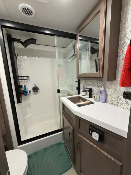 Modern RV rental bathroom featuring a sleek shower, vanity with sink, and toilet, complete with patterned wallpaper.. Grand Design Solitude 2024
