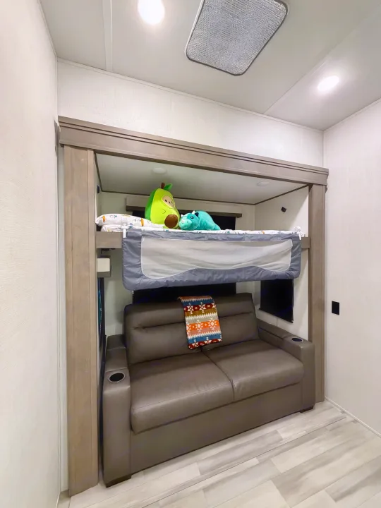 RV rental bunk bed with safety rail and plush toys above a comfortable leather sofa, ideal for family trips.. Grand Design Solitude 2024