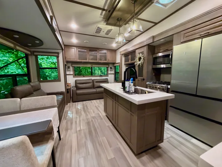 Modern RV rental interior with a spacious kitchen island, full appliances, cozy living area, and large windows with scenic views.. Grand Design Solitude 2024