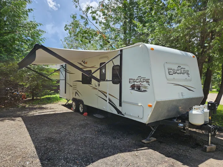 Enjoy outdoor adventure with this spacious RV rental. A white travel trailer with an extended awning under green trees.. Spree Escape 2014