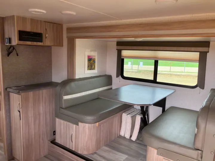 Inside an **rv rental**: Dinette with gray benches & table, adjacent to small kitchen area with cabinets & entertainment unit.. Winnebago Micro Winnie 2021