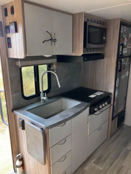Compact and functional RV rental kitchen featuring a sink, stove, microwave, fridge, and ample storage for travelers.. Winnebago Micro Winnie 2021