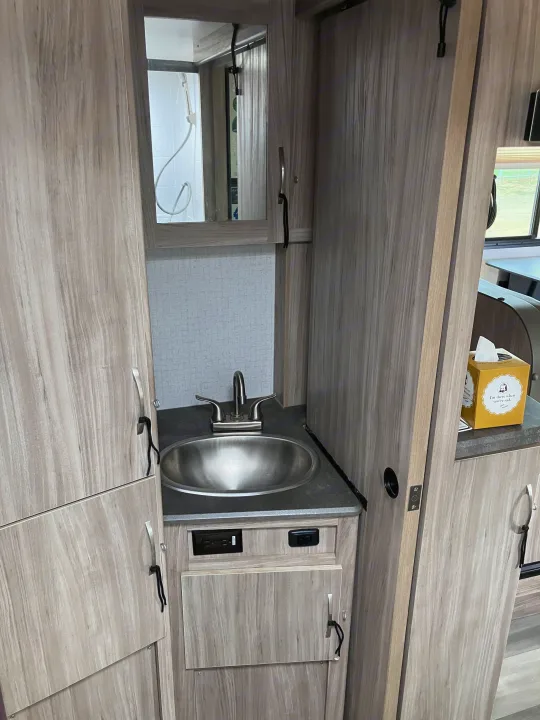 This rv rental features a compact bathroom vanity with a sink, faucet, mirror, and cabinet storage. Shower reflected.. Winnebago Micro Winnie 2021