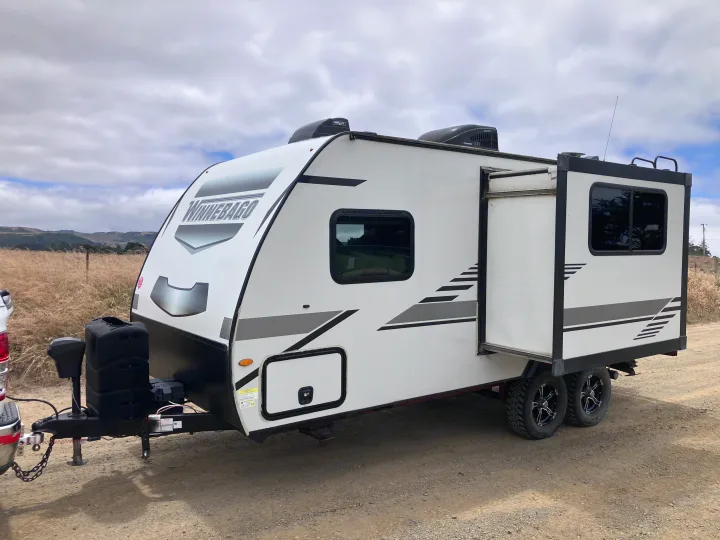 White Winnebago travel trailer on a gravel road, ready for your next rv rental camping trip amidst scenic hills.. Winnebago Micro Winnie 2021