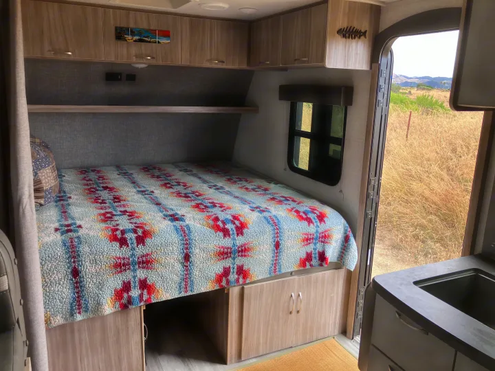 Cozy RV rental bedroom with colorful bed, storage, cabinets, and open door view of hills and dry grass.. Winnebago Micro Winnie 2021