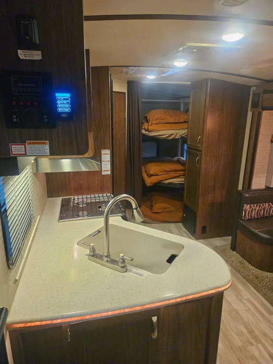 Inside an RV rental, showing the kitchen area with sink and stove, plus cozy bunk beds. A functional camper interior.. Dutchmen 242bhsl 2017