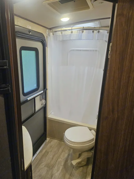 Compact RV rental bathroom features a shower with curtain, toilet, and an "EXIT" door. Perfect for on-the-go travelers.. Dutchmen 242bhsl 2017