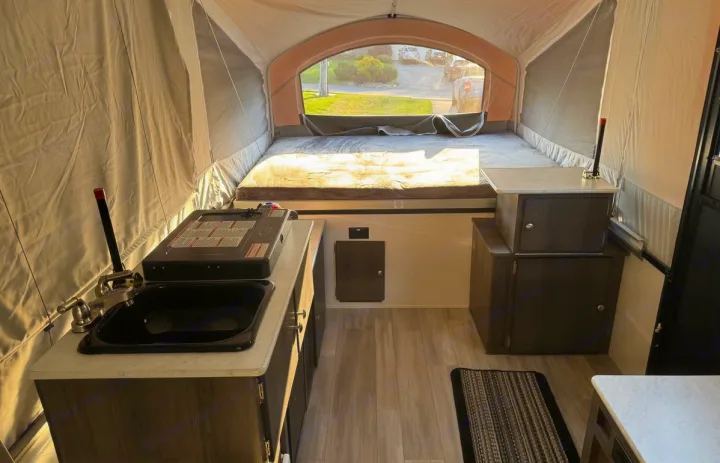 Inside this RV rental, a pop-up camper reveals a bed, compact kitchenette with sink & stove, and storage cabinets.. Forest River Viking LS 2022