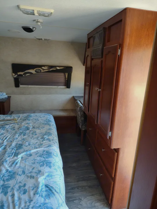 RV rental bedroom: a blue floral bed on the left, facing extensive wood cabinetry and a small desk on the right.. Fleetwood Terry 2007