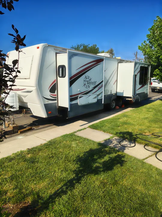White Terry RV rental, with extended slide-outs, parked by a grassy lawn on a clear, sunny day.. Fleetwood Terry 2007