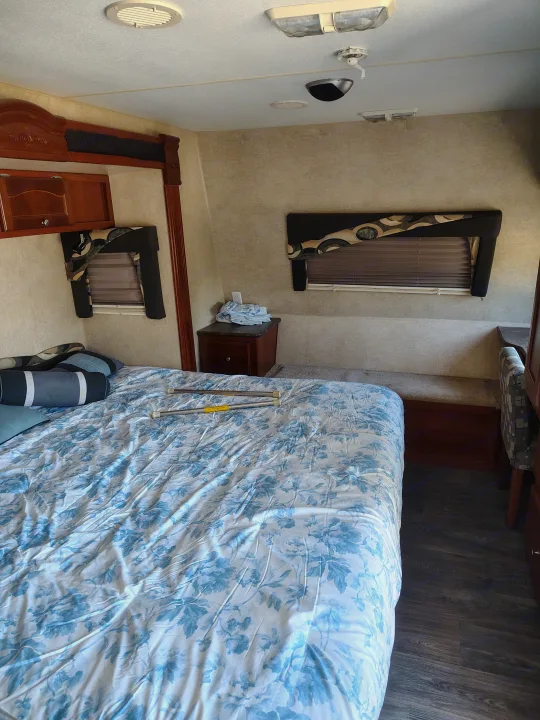 Inside an rv rental: a bedroom with a blue floral bedspread, wood cabinets, and blinds on windows, providing a cozy interior.. Fleetwood Terry 2007