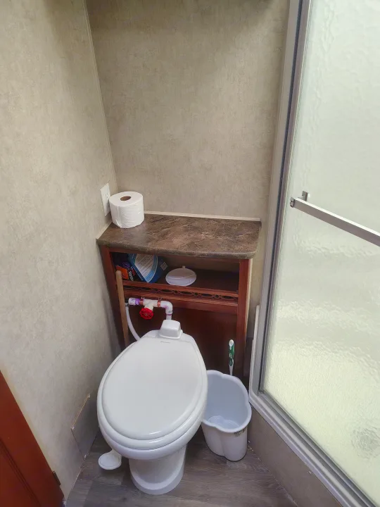 RV rental bathroom featuring a Dometic toilet, small counter with plumbing visible, storage, and a frosted shower stall.. Fleetwood Terry 2007