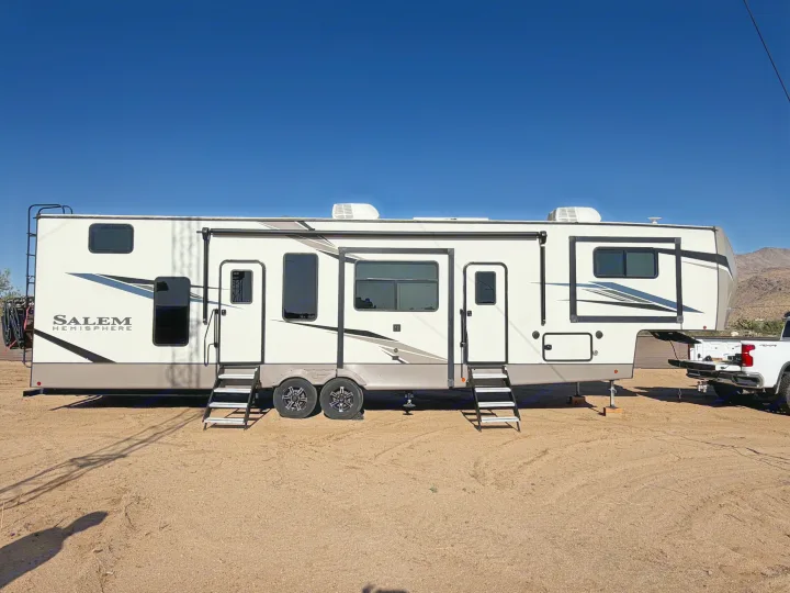 White Salem Hemisphere fifth-wheel RV rental, with steps & AC units, parked on dirt under clear blue sky.. Forest River Salem Hemisphere 2023