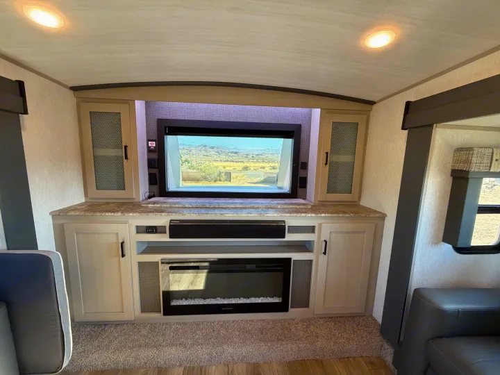 This RV rental features a well-equipped entertainment center: TV displaying outdoor scenery, electric fireplace, and ample storage cabinets.. Forest River Salem Hemisphere 2023