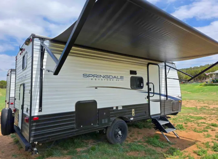 A white and black Springdale Keystone travel trailer with an extended awning and steps, perfect for an RV rental.. Keystone RV Springdale 2023