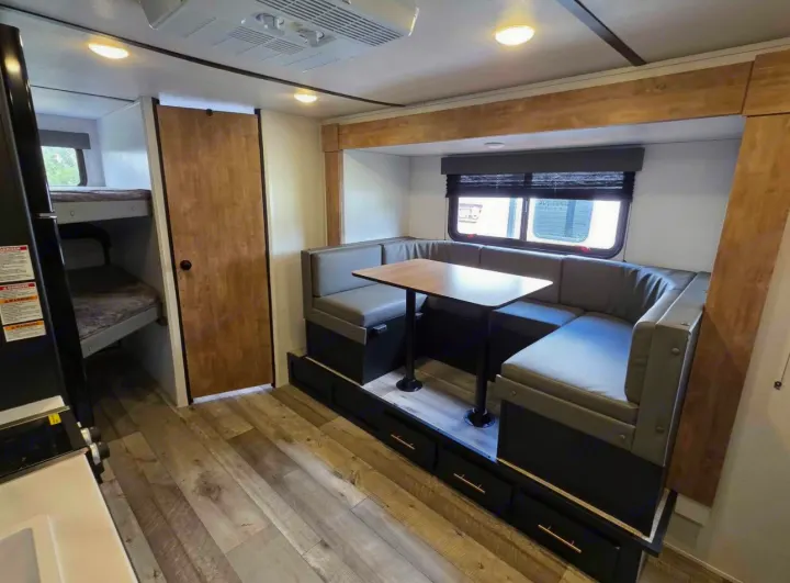 Spacious RV rental interior featuring a cozy U-shaped dinette, bunk beds, and modern wood flooring. Perfect for family adventures.. Keystone RV Springdale 2023