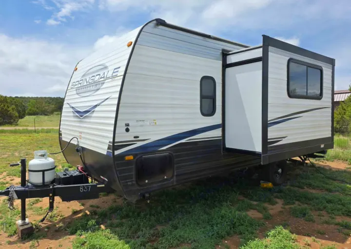 RV rental: A white Springdale travel trailer with blue stripes and an extended slide-out, parked on grass.. Keystone RV Springdale 2023