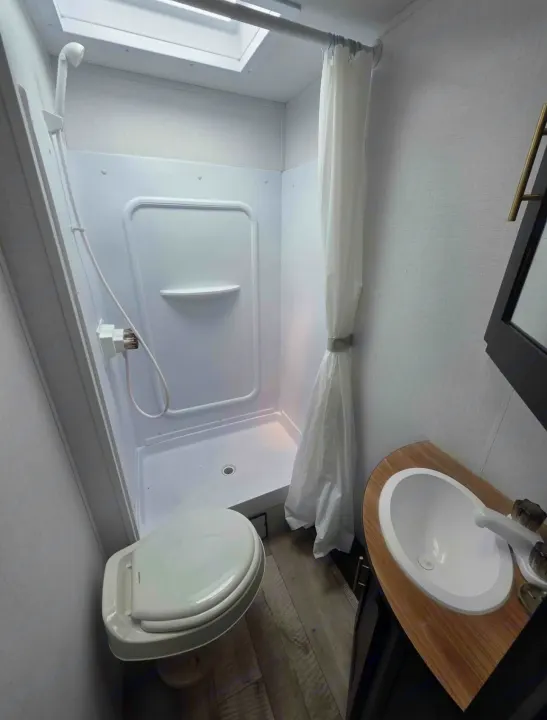 RV rental: Compact, bright bathroom with a white shower, toilet, and sink, including a skylight.. Keystone RV Springdale 2023