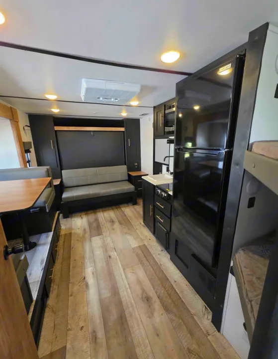 Modern RV rental interior with black kitchen, dining, sofa, and bunk beds. Light wood floors and sleek design.. Keystone RV Springdale 2023