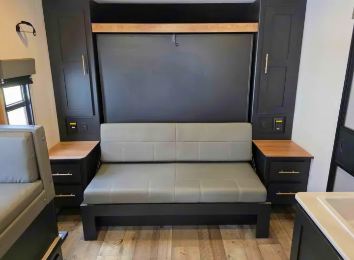 RV rental's modern interior: gray sofa, folded wall bed, black cabinets with wood accents and built-in storage.. Keystone RV Springdale 2023