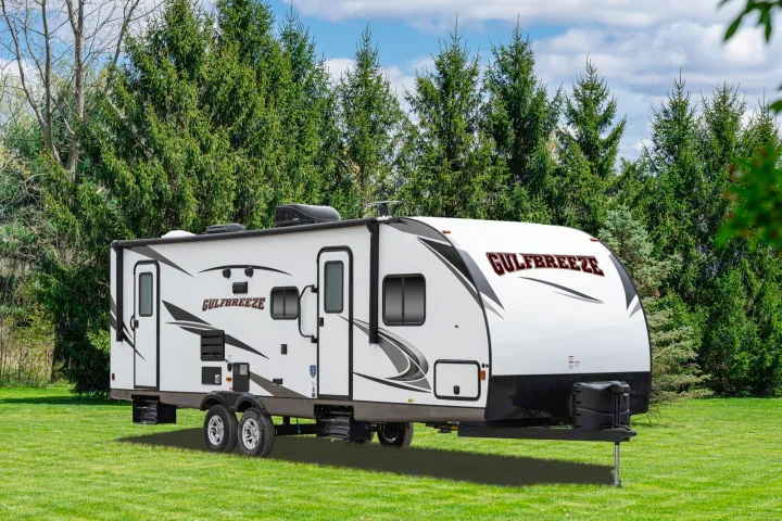 A white Gulf Breeze travel trailer, ideal for RV rental and outdoor trips, sits on green grass before tall pine trees.. Gulf Stream Envision 2025