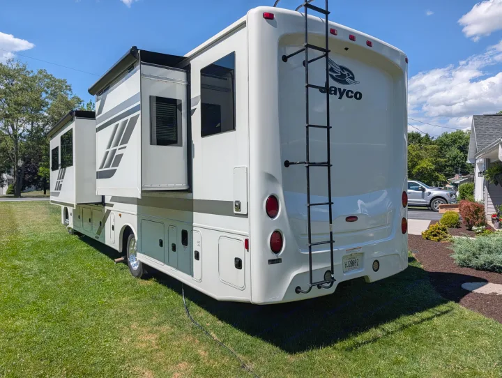 Rear and side view of a white Jayco rv rental (motorhome) with slide-outs open, parked on a sunny green lawn.. Jayco Precept 2025