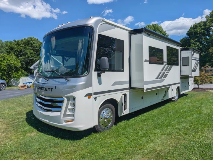 A sleek white and silver RV rental with extended slide-outs, parked on lush green grass on a sunny day.. Jayco Precept 2025