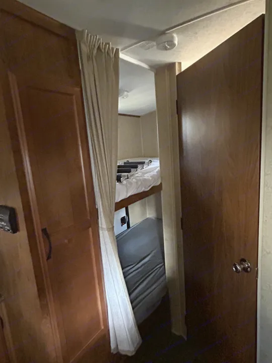 RV rental interior showing a compact bunk bed area (top bed with white bedding, lower with gray mattress), a cabinet, and a door.. Outdoors RV 22BHS 2019